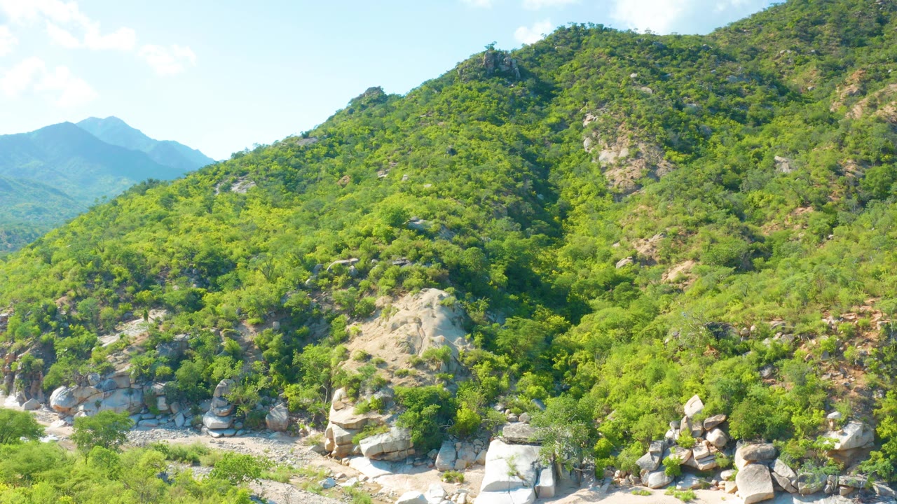 Opening view of green mountain slopes and pale boulders in La Palma, Baja California Sur, Mexico, with distant blue ridges and no visible people.