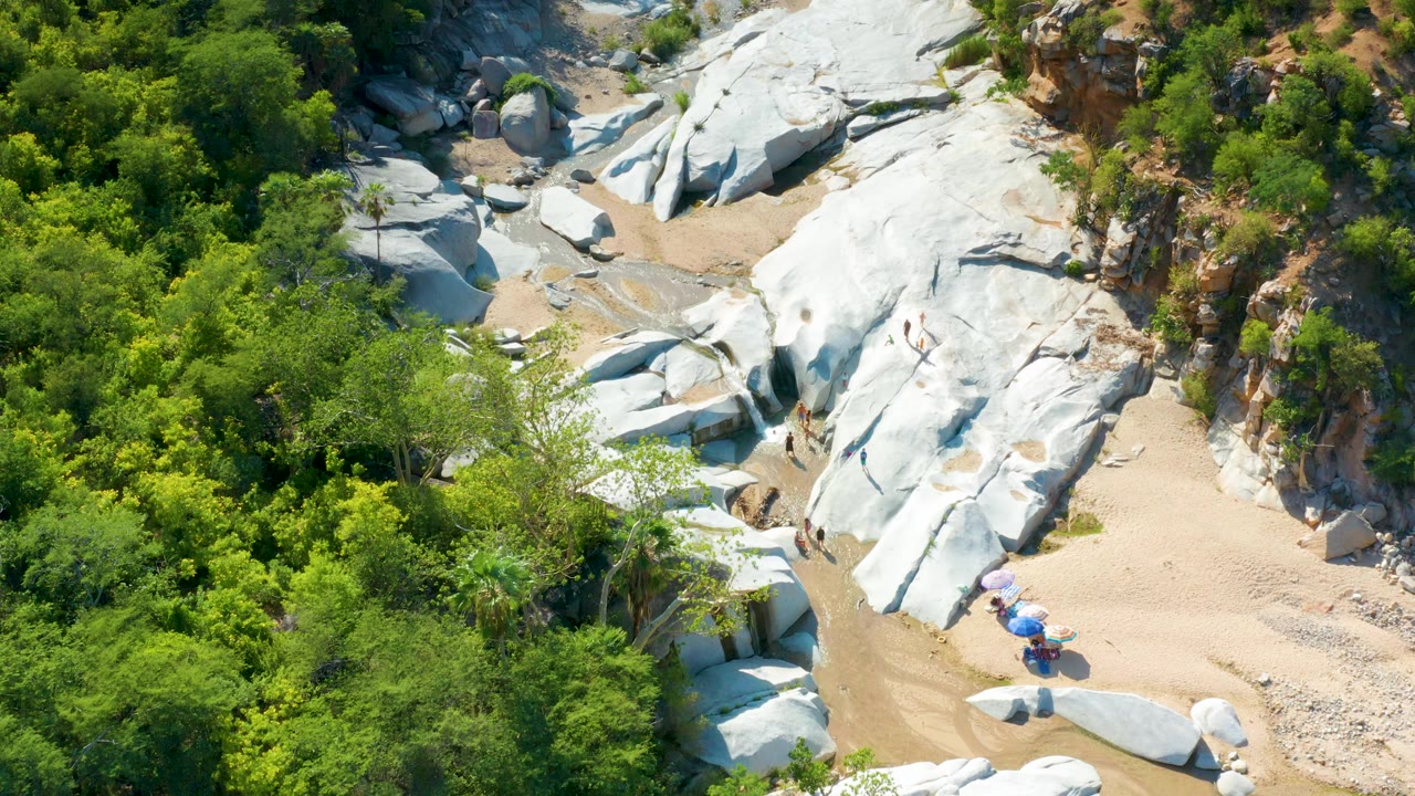 Aerial frame in La Palma, Baja California Sur, with white rock slabs running diagonally through tan sand and green brush, with no visible people.