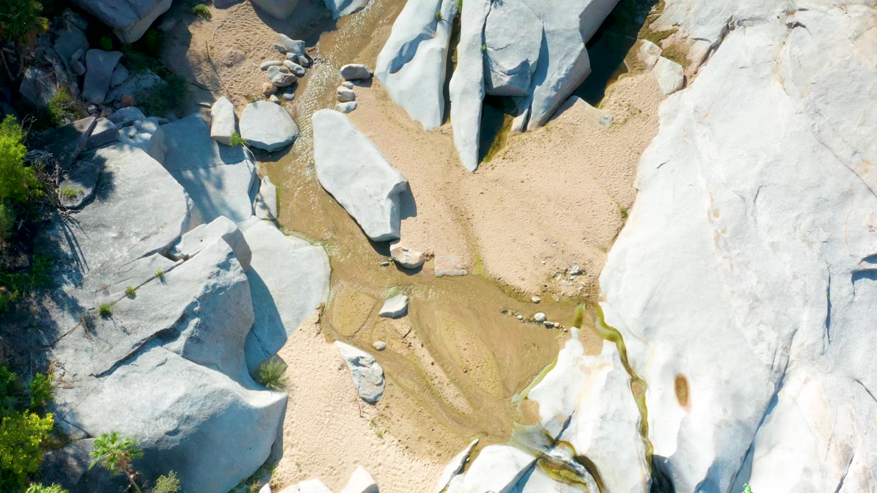 Aerial-looking view in La Palma, Baja California Sur with a central sandy wash, rounded white boulders, darker shrub edges, and no visible people.