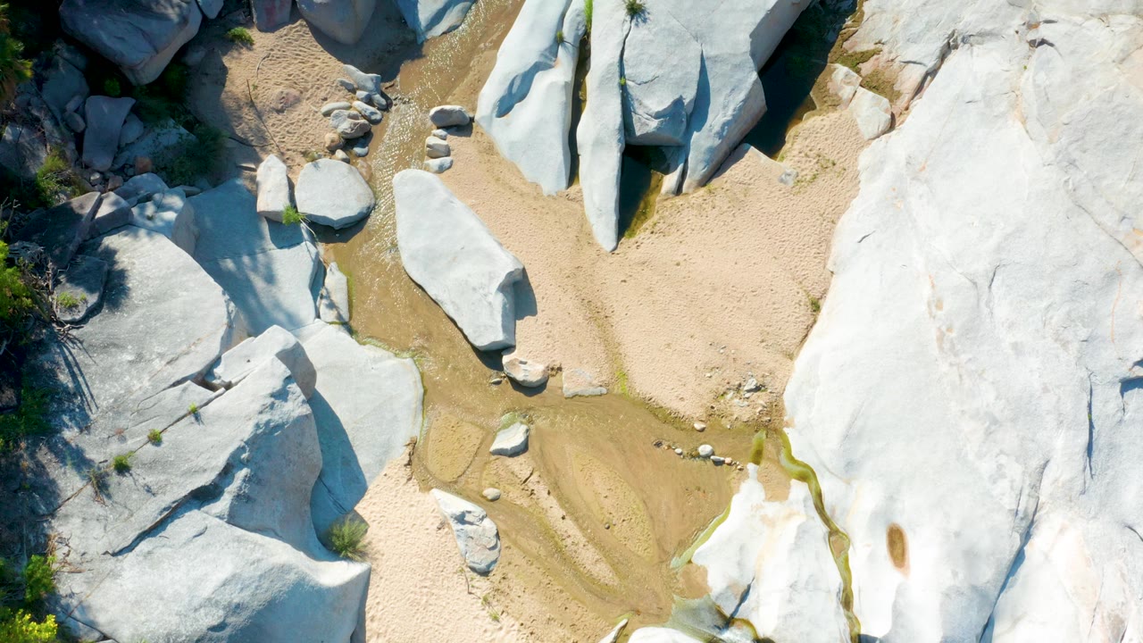 Overhead La Palma, Baja California Sur frame with a broad pale rock slab on the right, clustered stones near the sandy center, and no visible people.