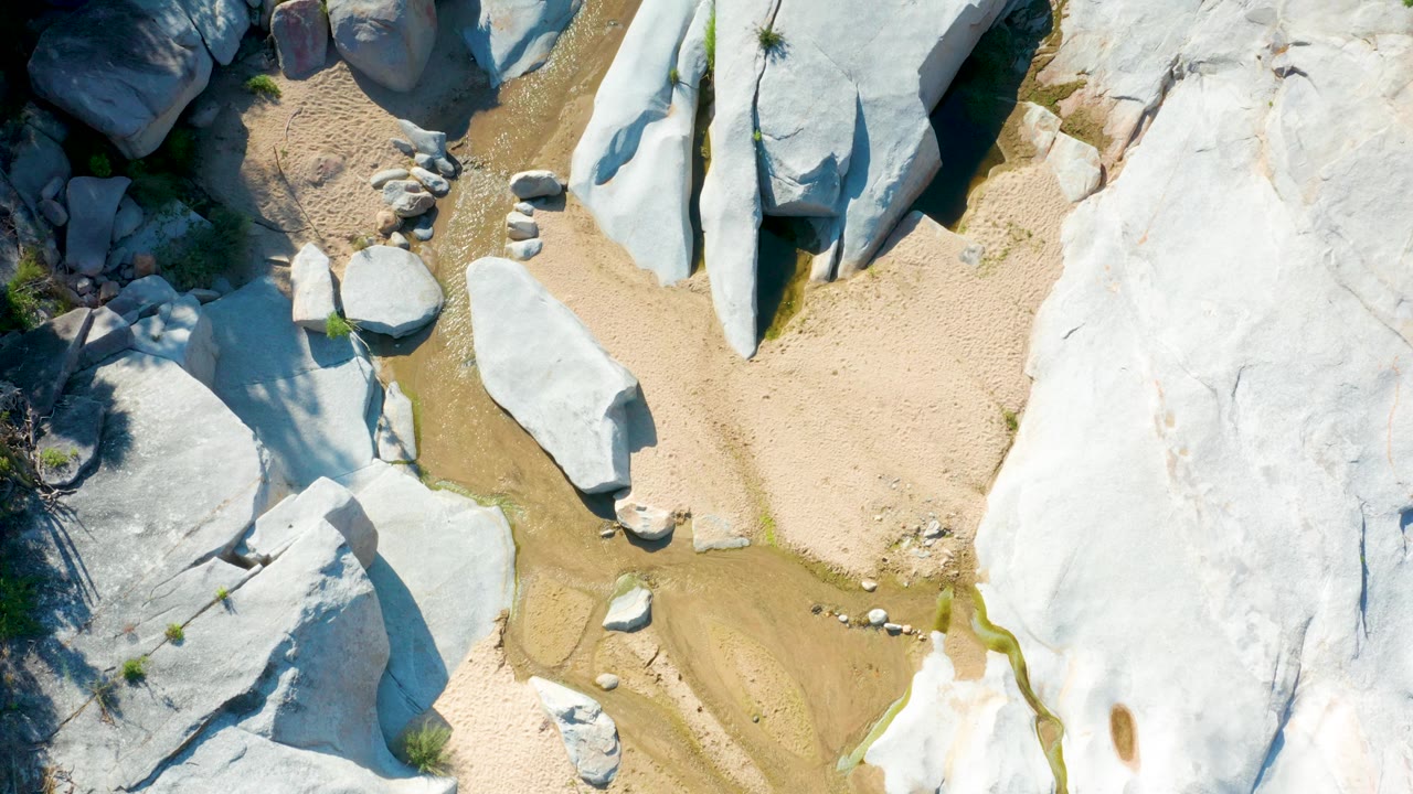 Pale boulders and sand seen from directly above.