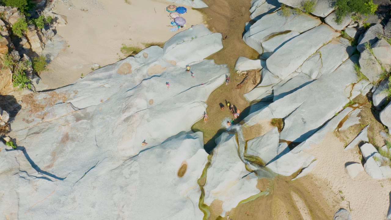 Aerial view of white rock shelves with people near a narrow water channel.