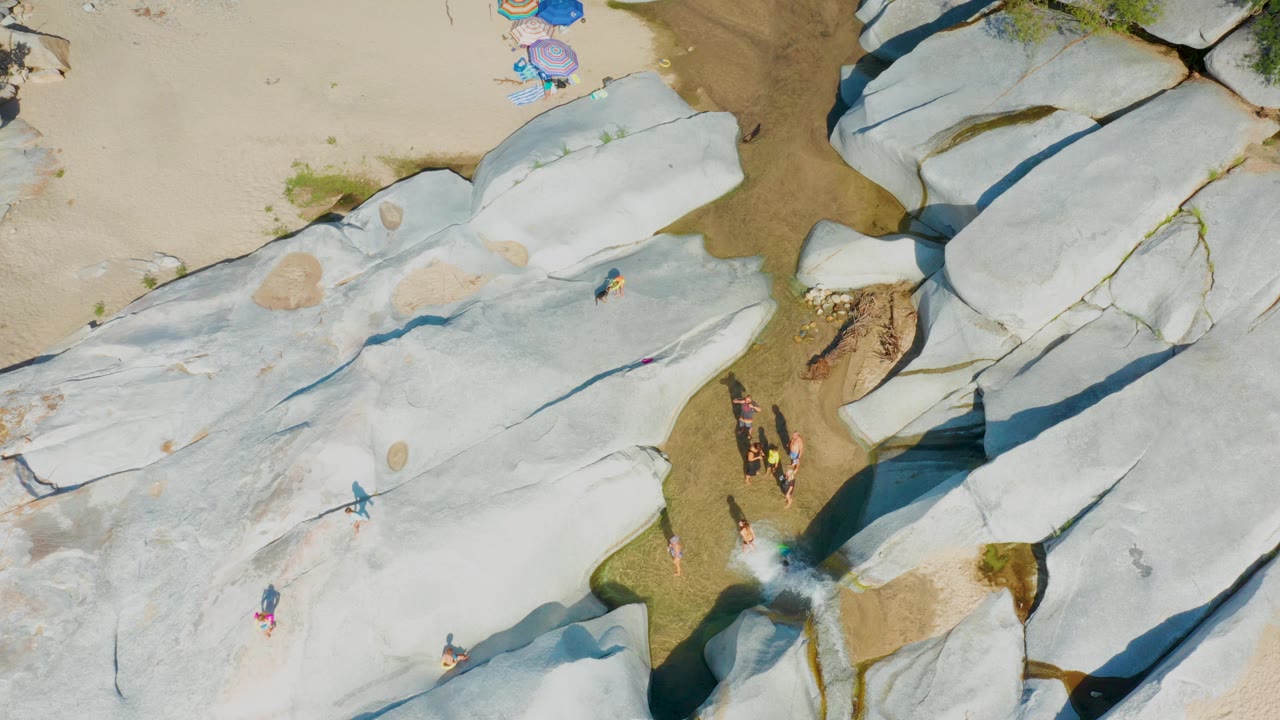 Top-down pale rock formation with people near a wet channel.