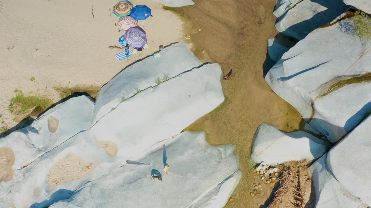 Overhead view of beach umbrellas beside shallow water and large pale rocks.