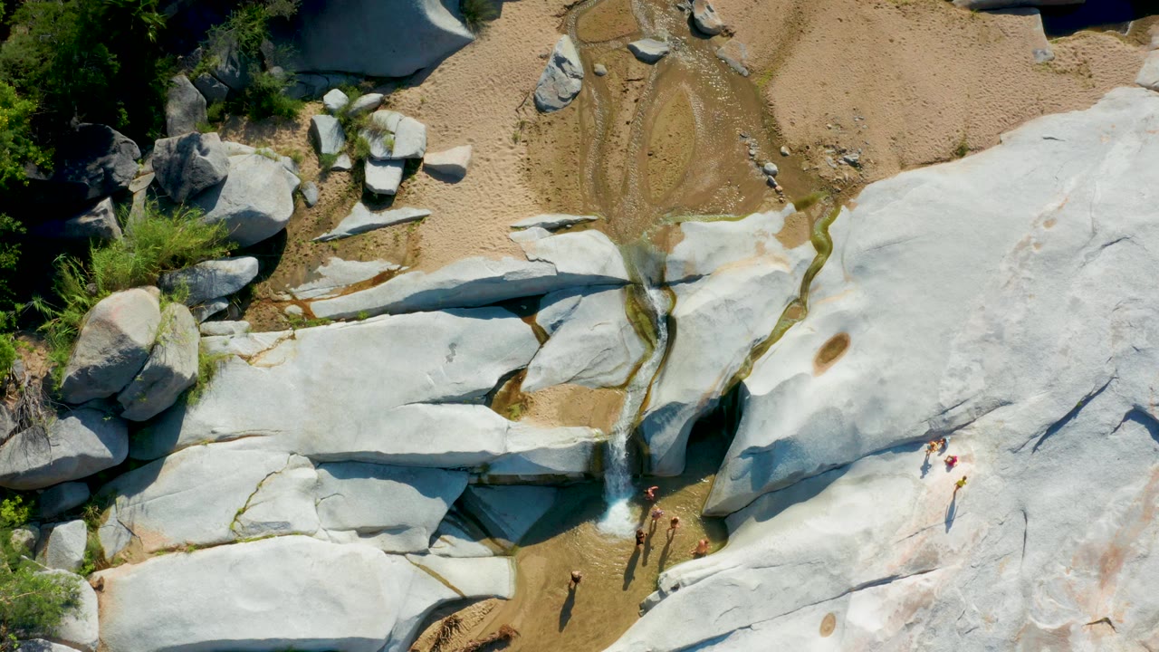 Aerial view of a narrow waterfall running through pale rock with people nearby.