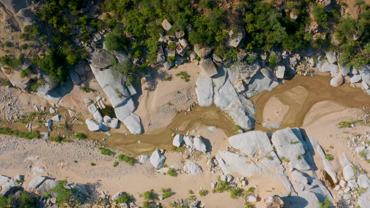 Aerial view of a sandy channel curving between boulders and trees.