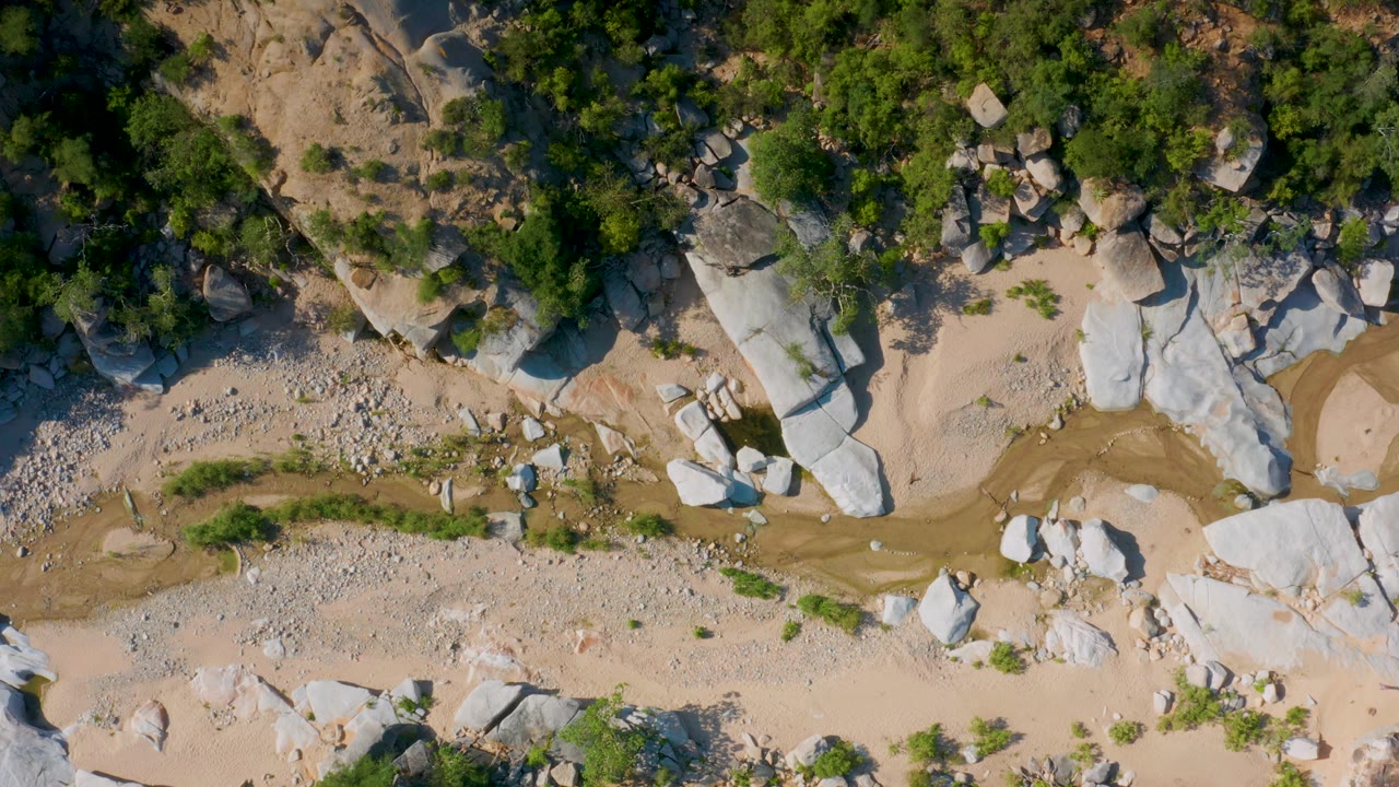 Overhead view of a rocky wash with white boulders, sand, shrubs, and scattered pebbles.