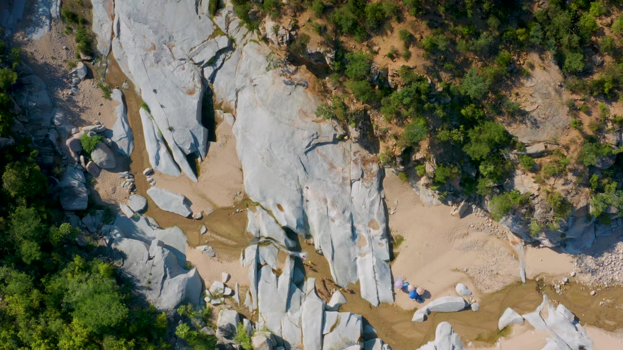 Overhead view of a sandy creek bed crossing pale rock and green trees.
