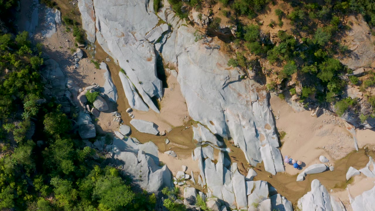Aerial view in La Palma, Baja California Sur, with elongated white rock forms crossing a sandy wash, green brush around the edges, and no visible people.