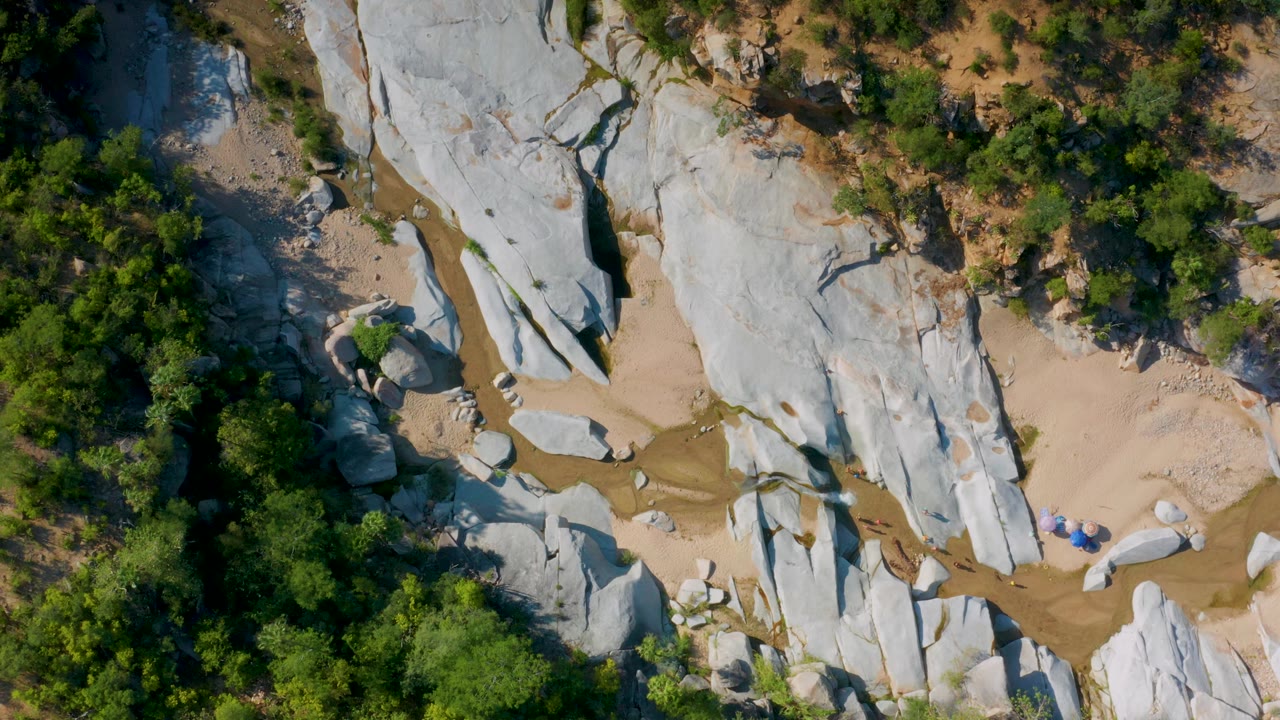 Overhead La Palma, Baja California Sur frame with smooth white rock surfaces, a narrow sandy creek bed, green trees on both sides, and no visible people.