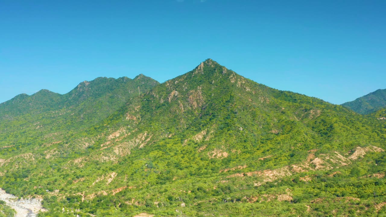 A broad hillside in La Palma, Baja California Sur, shows green vegetation, tan exposed rock, layered ridges, and no visible people.