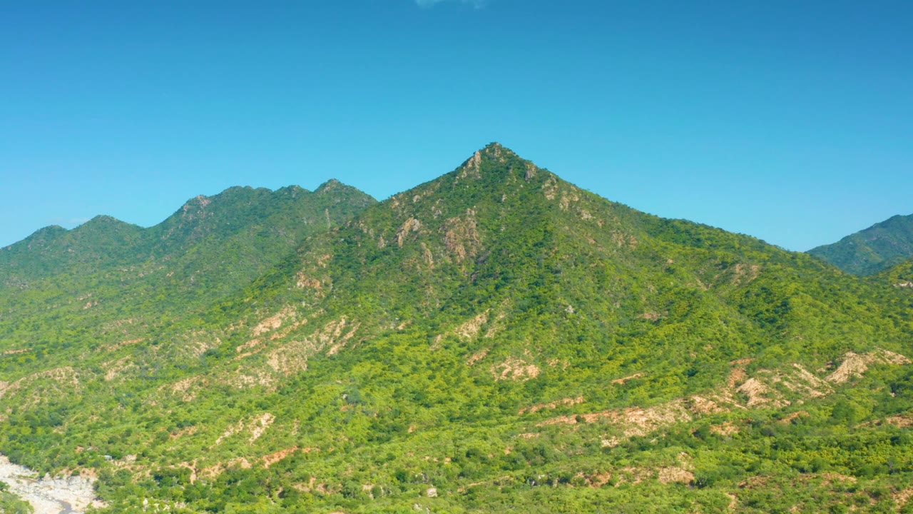 The La Palma hillside remains centered, with a steeper rocky peak, green scrub cover, distant blue-green ridges, and no visible people.