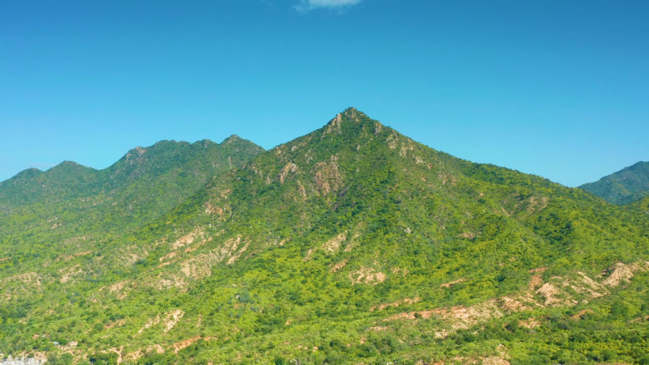 A broad green slope with pale exposed rock crosses the foreground, backed by darker ridgelines in La Palma, Baja California Sur, Mexico, with no visible people.
