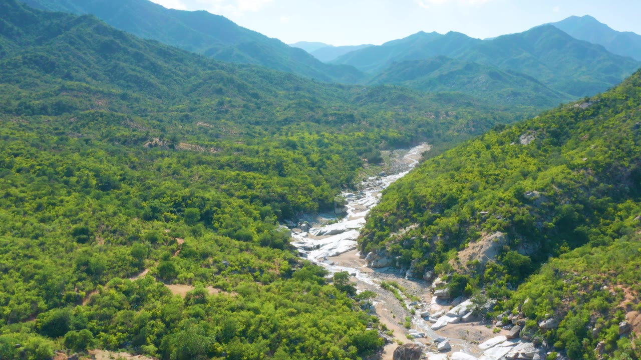 Aerial landscape of green hills with a winding rocky creek in the valley floor.