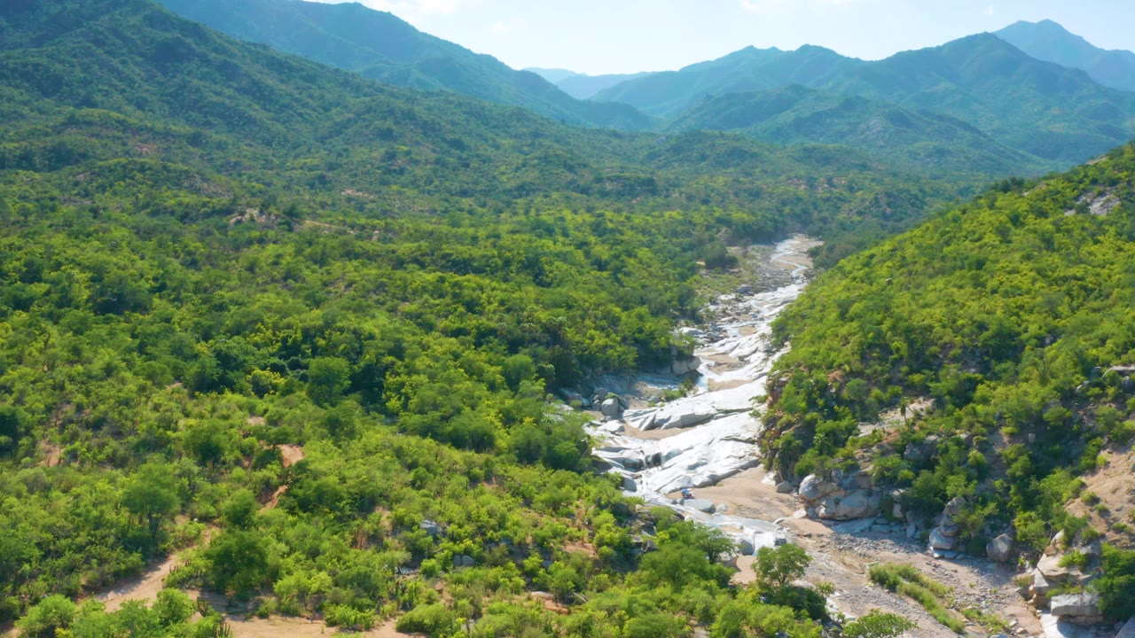 Wide drone view of shrubs, hills, and exposed creek rocks