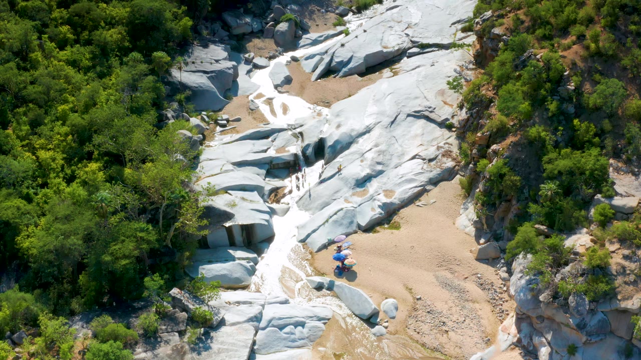 Aerial view over white rock shelves, sand, brush, and people by umbrellas.