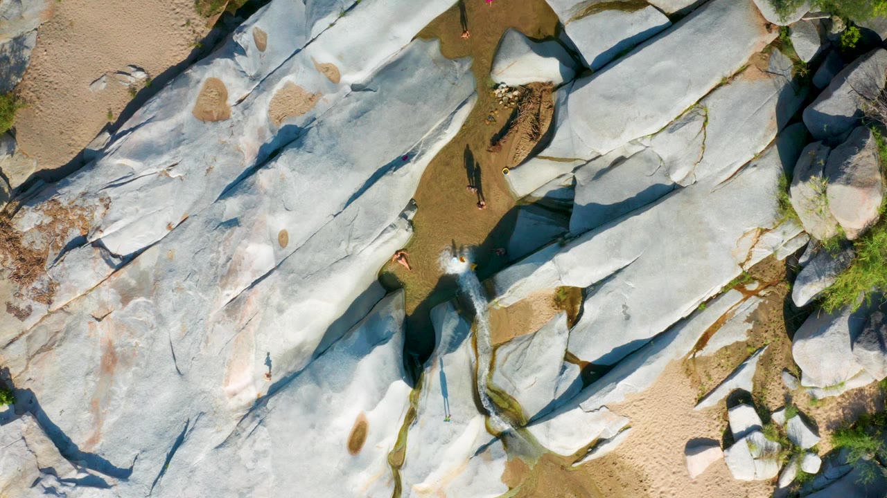 Aerial view of smooth rock with water passing through a narrow sandy gap.
