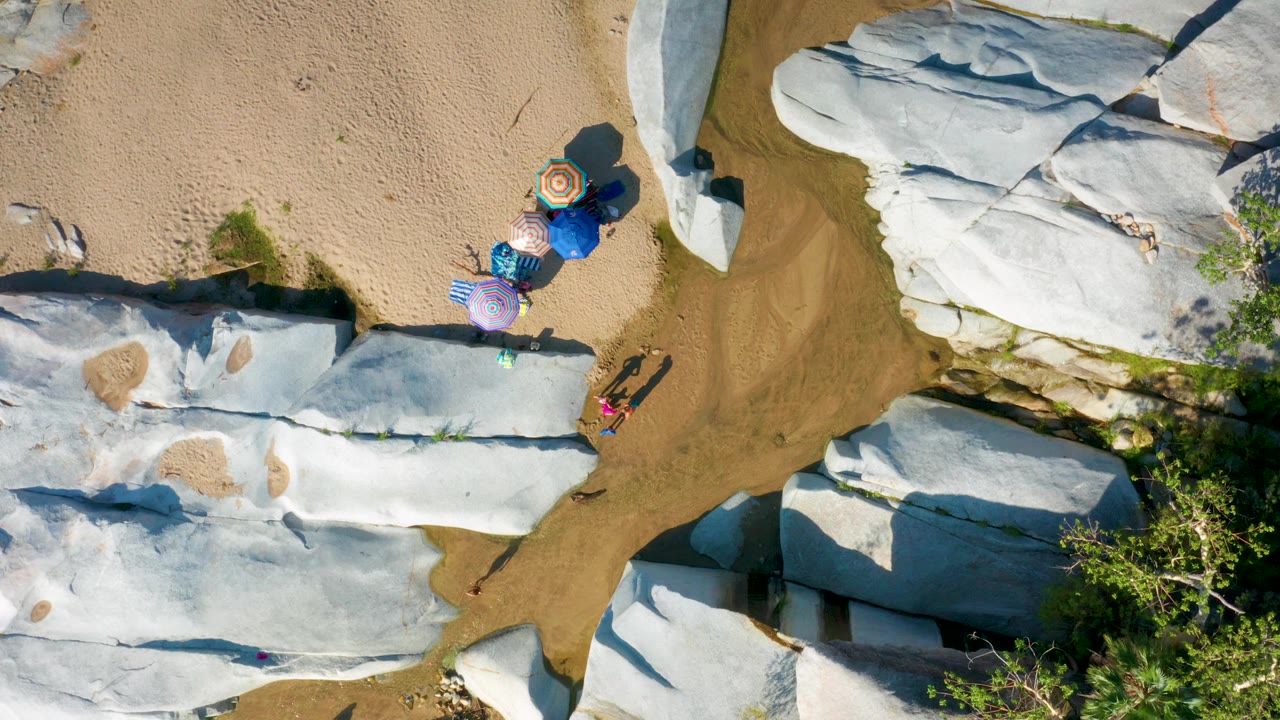 Overhead view of beach umbrellas near pale rocks and shallow water.