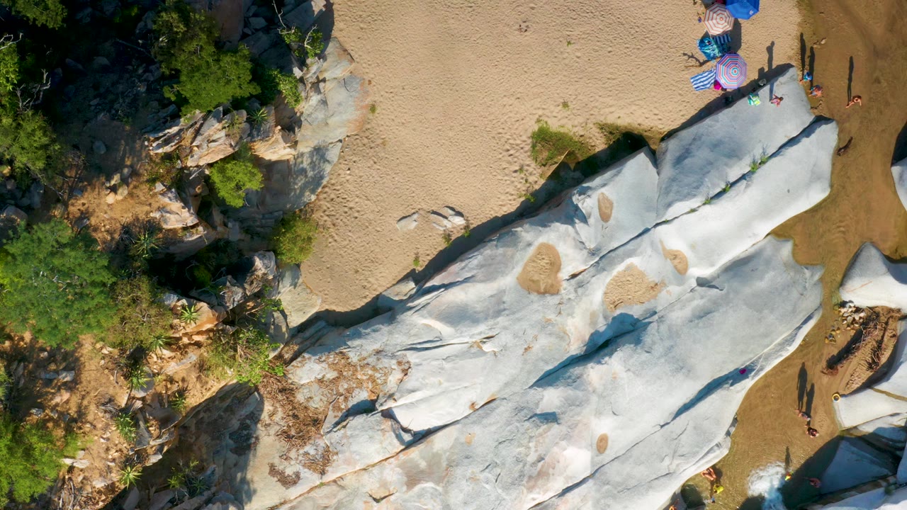 Top-down view of white rock slabs beside sand and sparse greenery.
