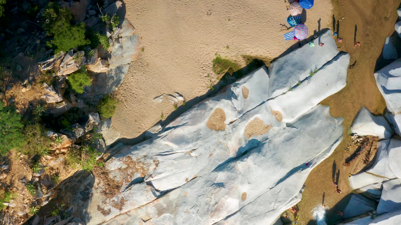 Overhead rocks and sand with greenery and small figures at the edge.