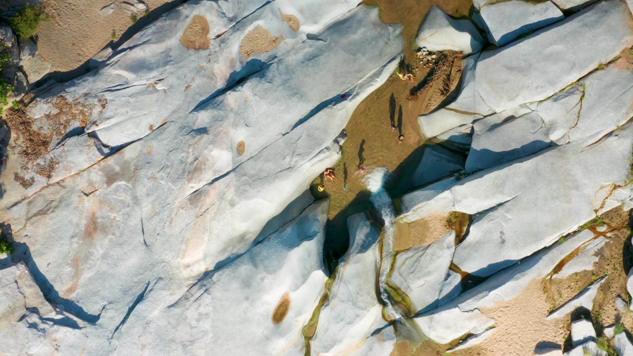 Pale rock slabs and sand viewed from above with people at lower center.