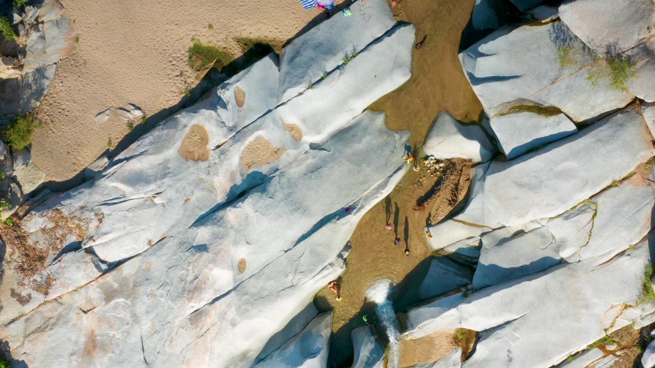 Aerial view in La Palma, Baja California Sur, with large white stone plates, darker cracks, tan patches, a brown water channel near the upper edge, and no clearly visible people.