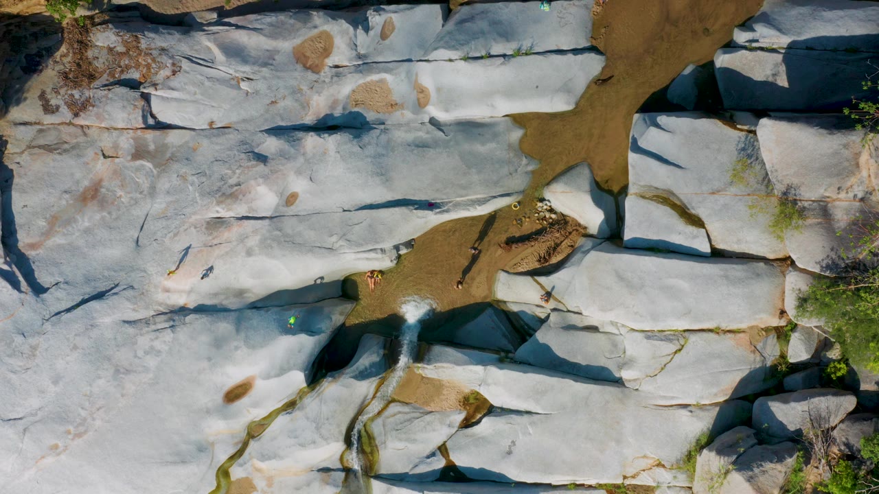 Aerial view of white rock shelves with a narrow sandy wash and small figures.