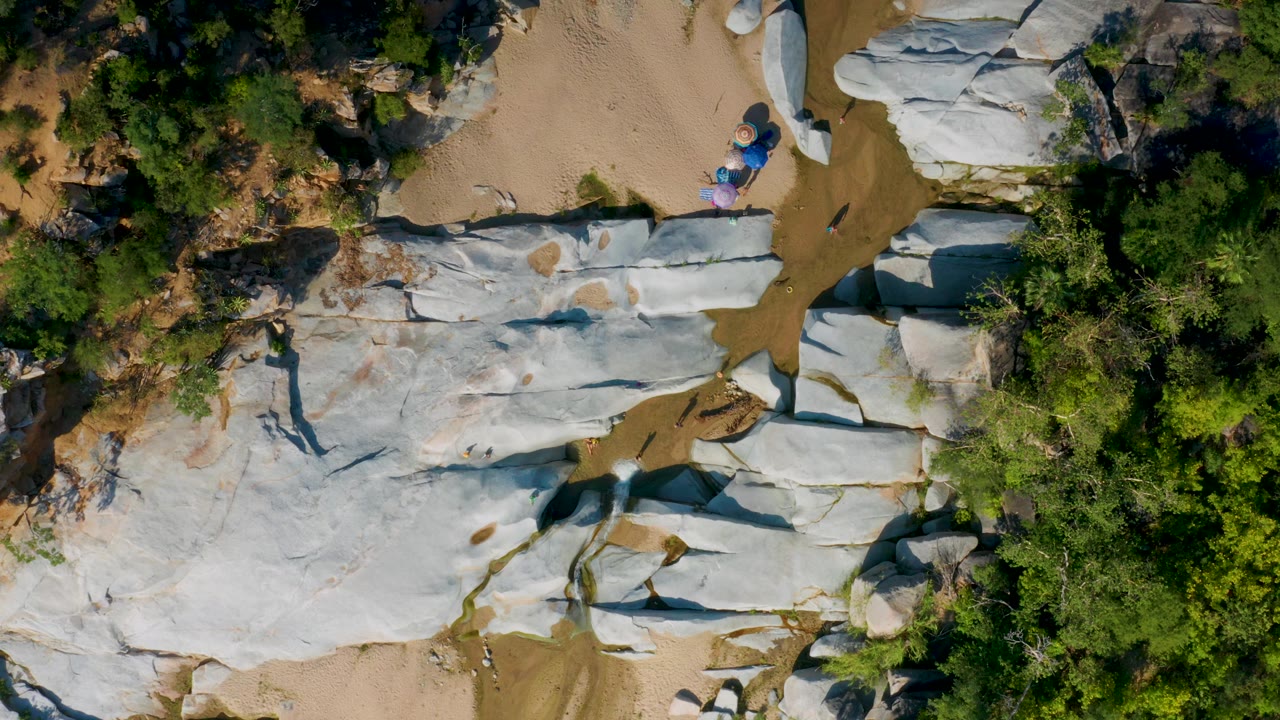 Top-down rocky wash with trees and small people near colorful items.