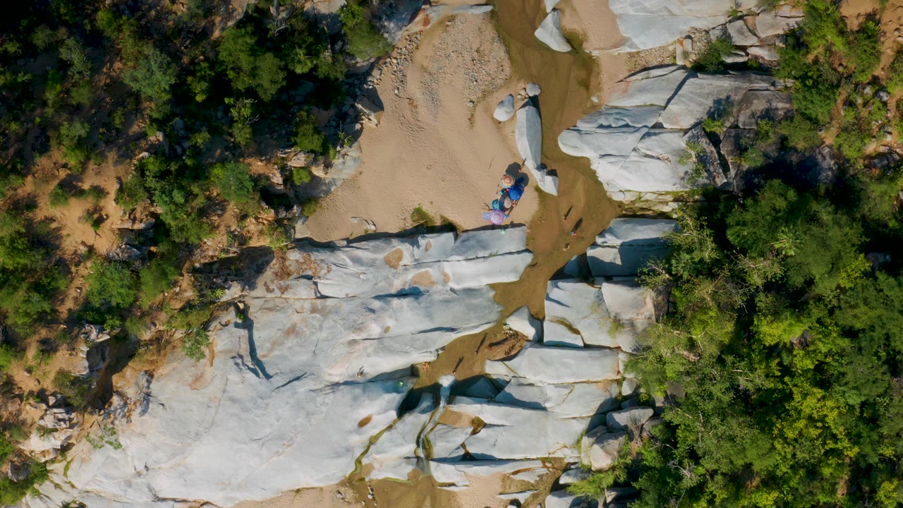 Aerial view of white rock shelves beside dense trees and a sandy creek bed.