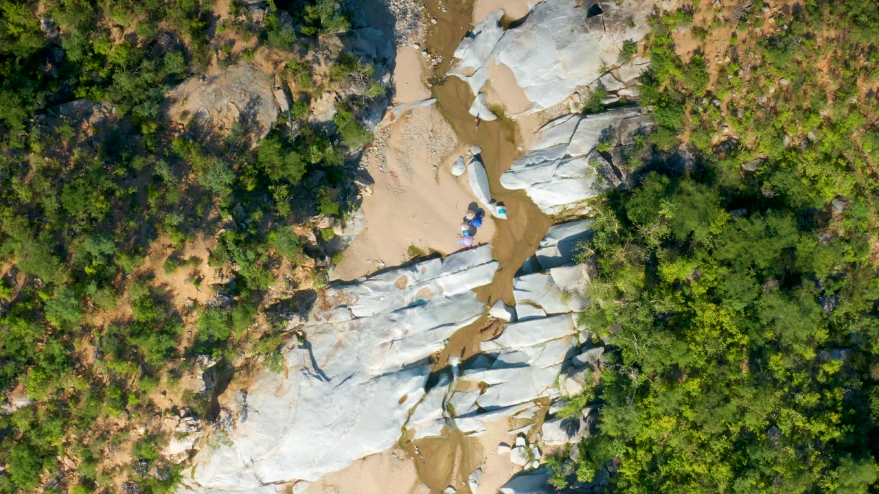 Top-down frame of pale stone formations, tan river sand, and surrounding forest.