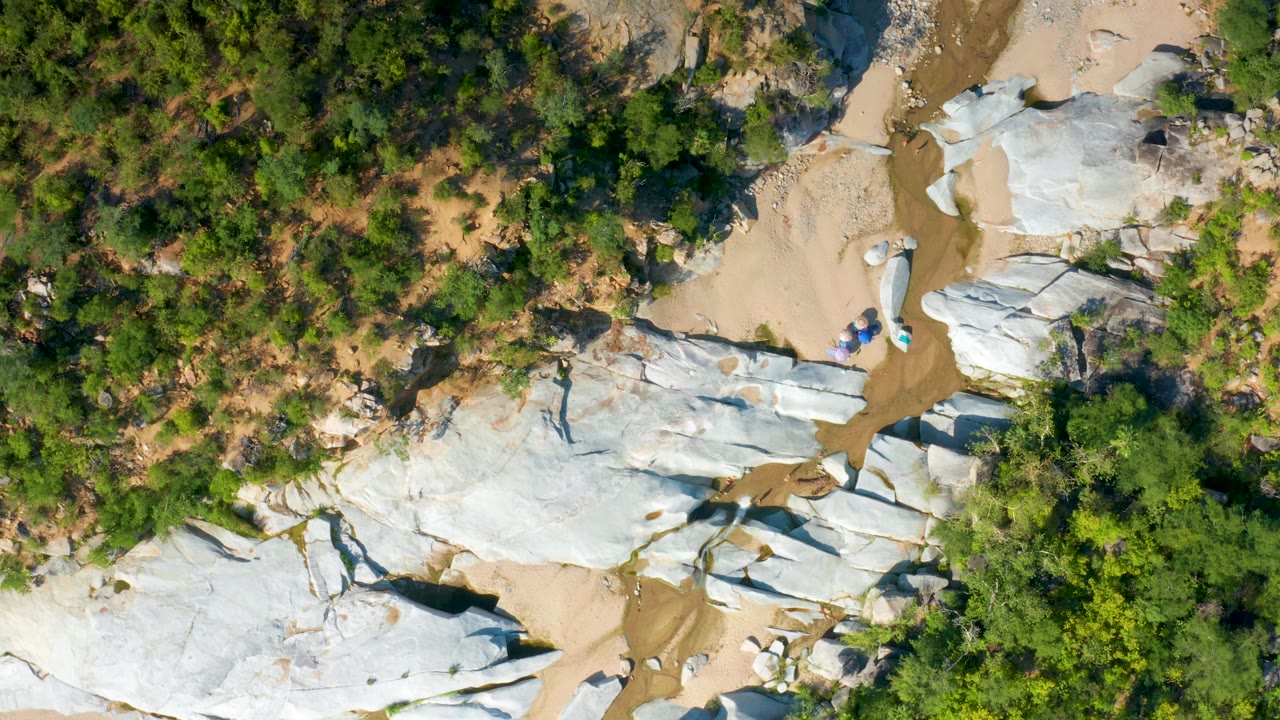 Top-down La Palma, Baja California Sur frame showing a sandy wash winding between pale rocks and scrubby green vegetation, with no visible people.