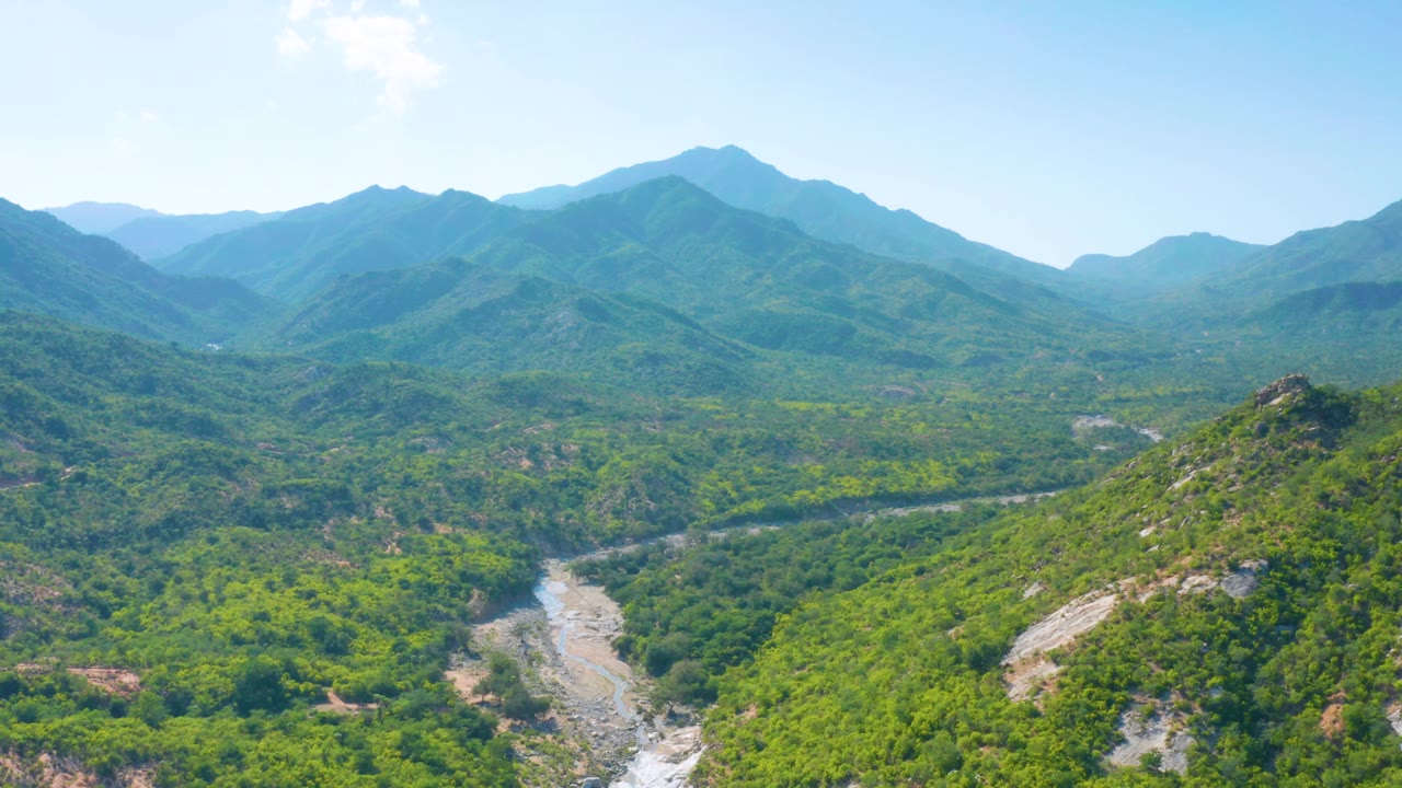 Drone view across a green valley with layered mountain ridges.