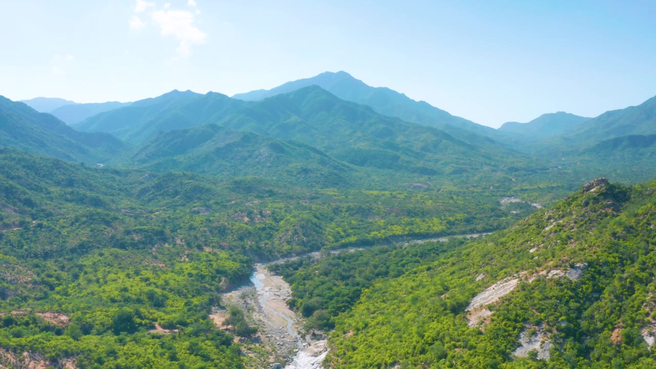 La Palma aerial panorama with a central green ridge, pale rock exposed along the lower slope, distant mountain layers, bright sky, and no visible people.
