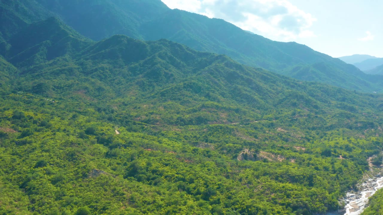 Aerial view in La Palma, Baja California Sur, with the central ridge line prominent, green vegetation across the valley, hazy blue hills in back, a riverbed at lower right, and no visible people.