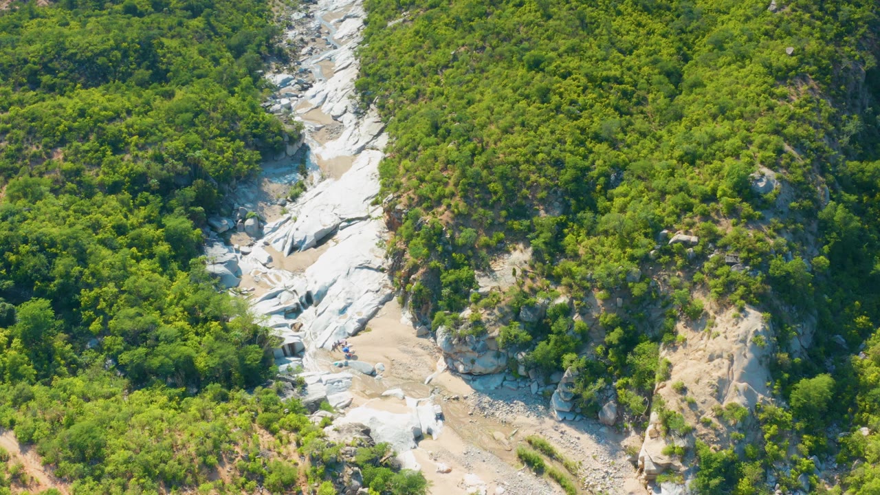 Rocky wash and green hillside seen from above.