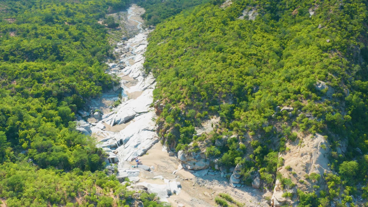 Aerial view in La Palma, Mexico with the arroyo centered lower in frame and green slopes rising on both sides, with no visible people.
