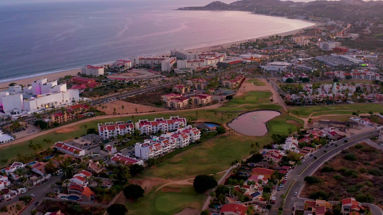 Aerial coastline with fairways, buildings, road traffic, and low evening light