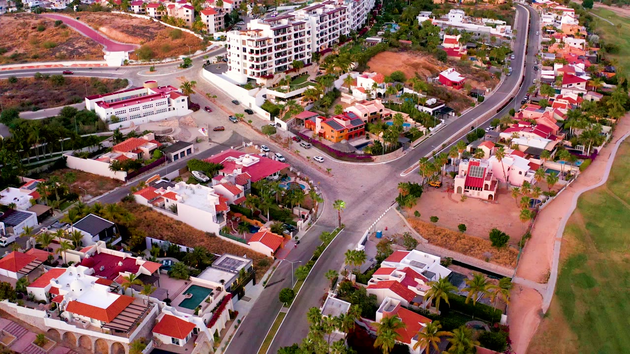 Overhead neighborhood angle with red-tiled houses, parking areas, roads, and hillside development.