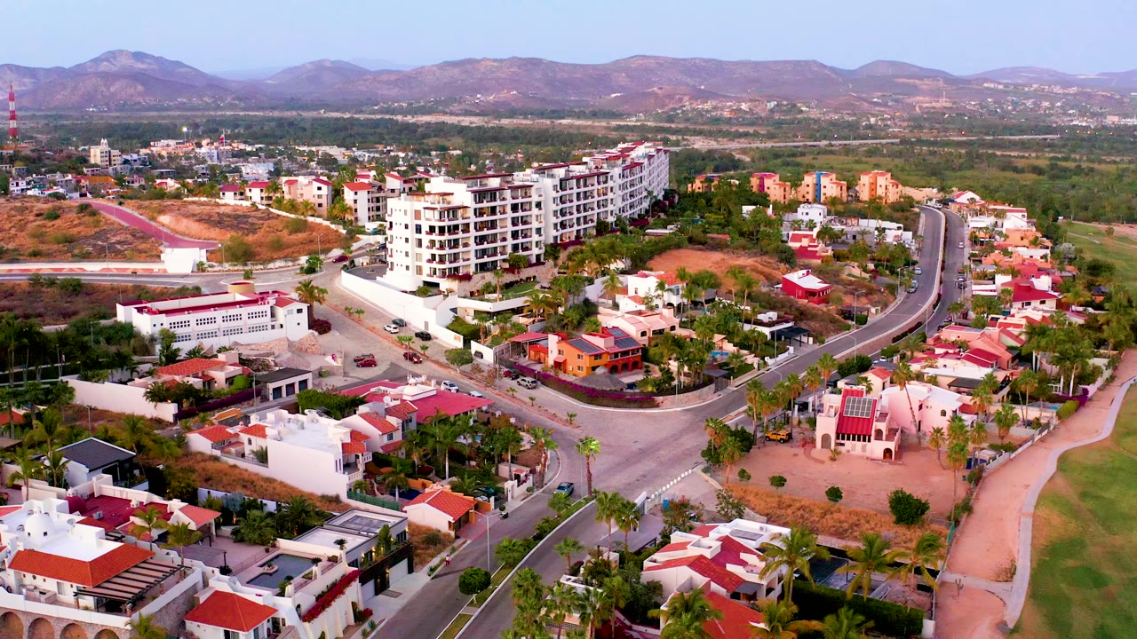 Drone view of homes, road intersections, palms, and distant hills.