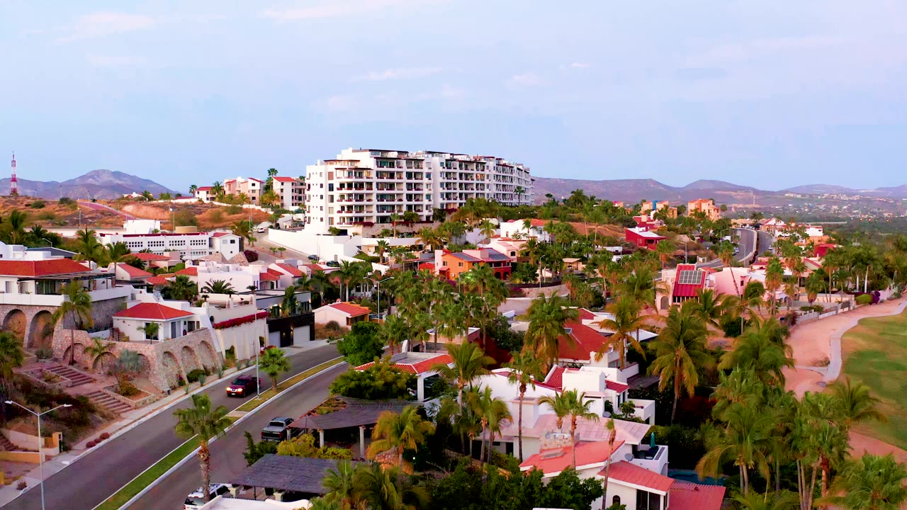 Residential street with palms, white buildings, red roofs, and hills
