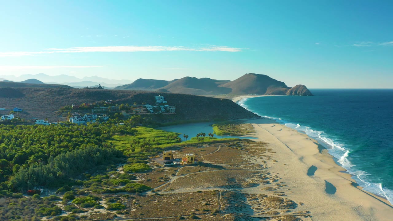 Elevated coastline view with green vegetation, lagoon, sandy beach, surf, and hills.