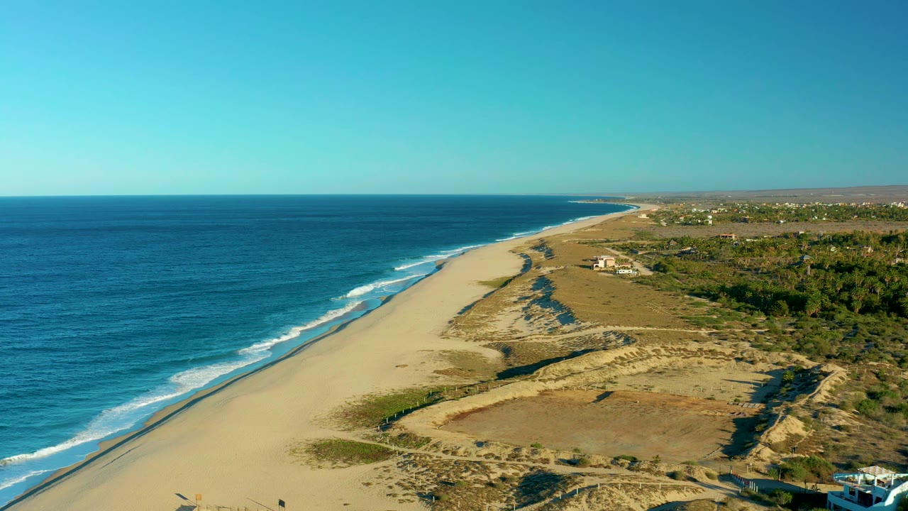Blue ocean waves run beside a broad sand beach and dune area.
