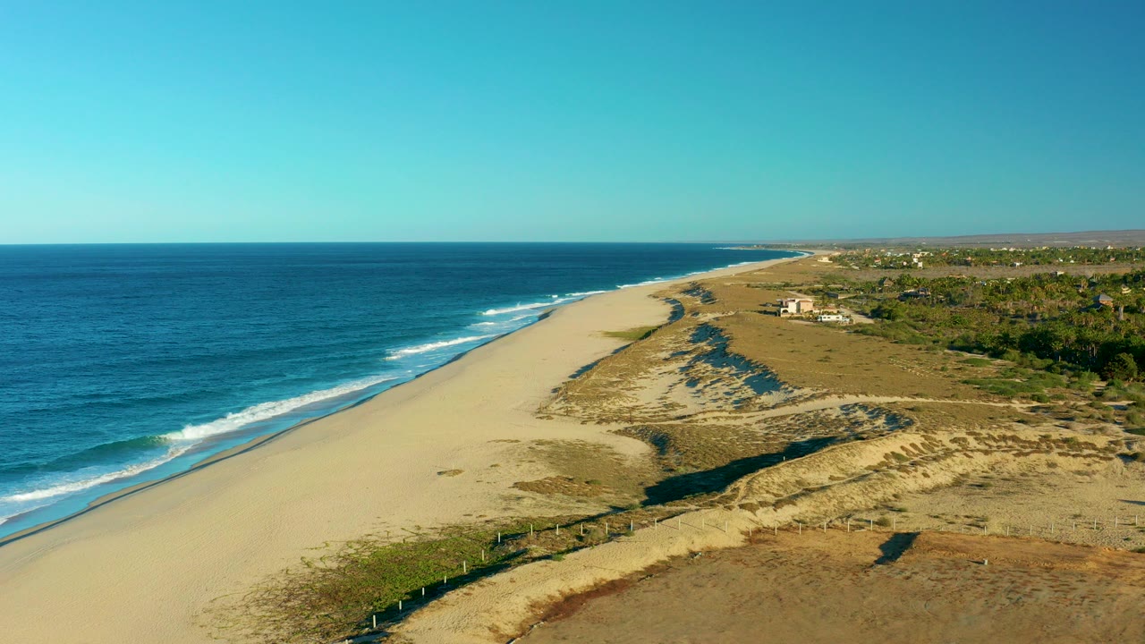 Aerial view of Todos Santos, Baja California Sur coastline with blue ocean at left, broad sand and dune ridges to the right, and no visible people.