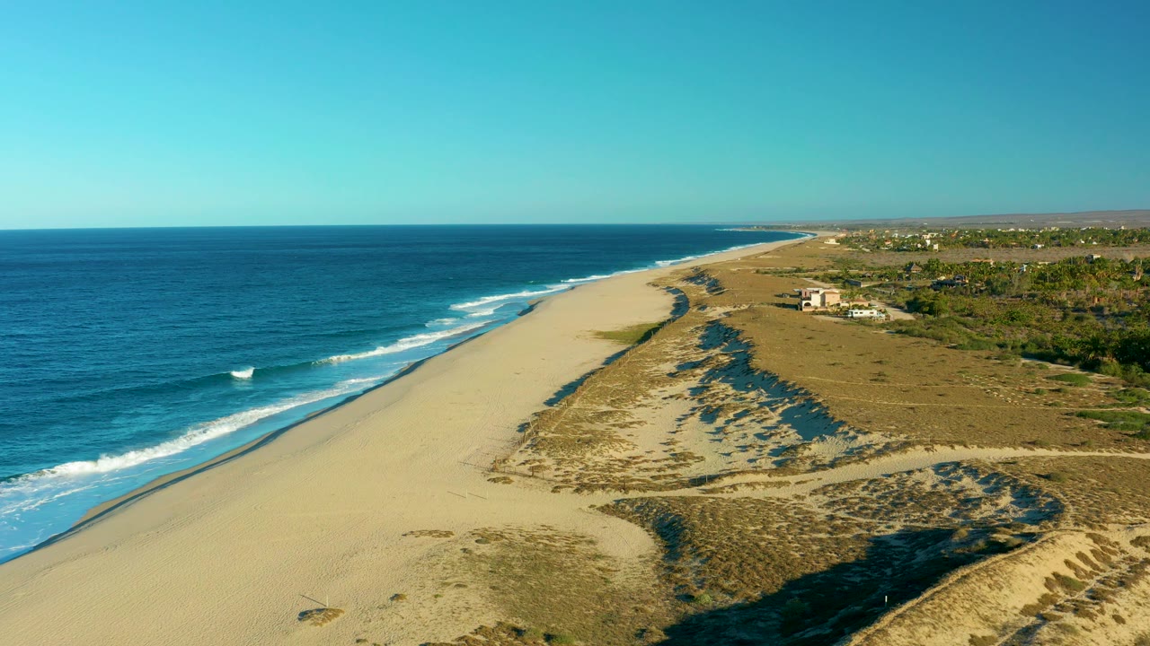 Ocean surf and empty beach with dunes casting long shadows.