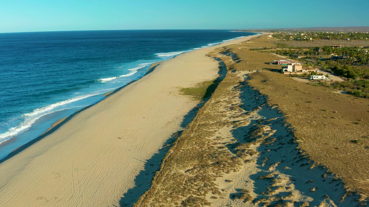 Ocean surf curves beside empty sand and dune vegetation