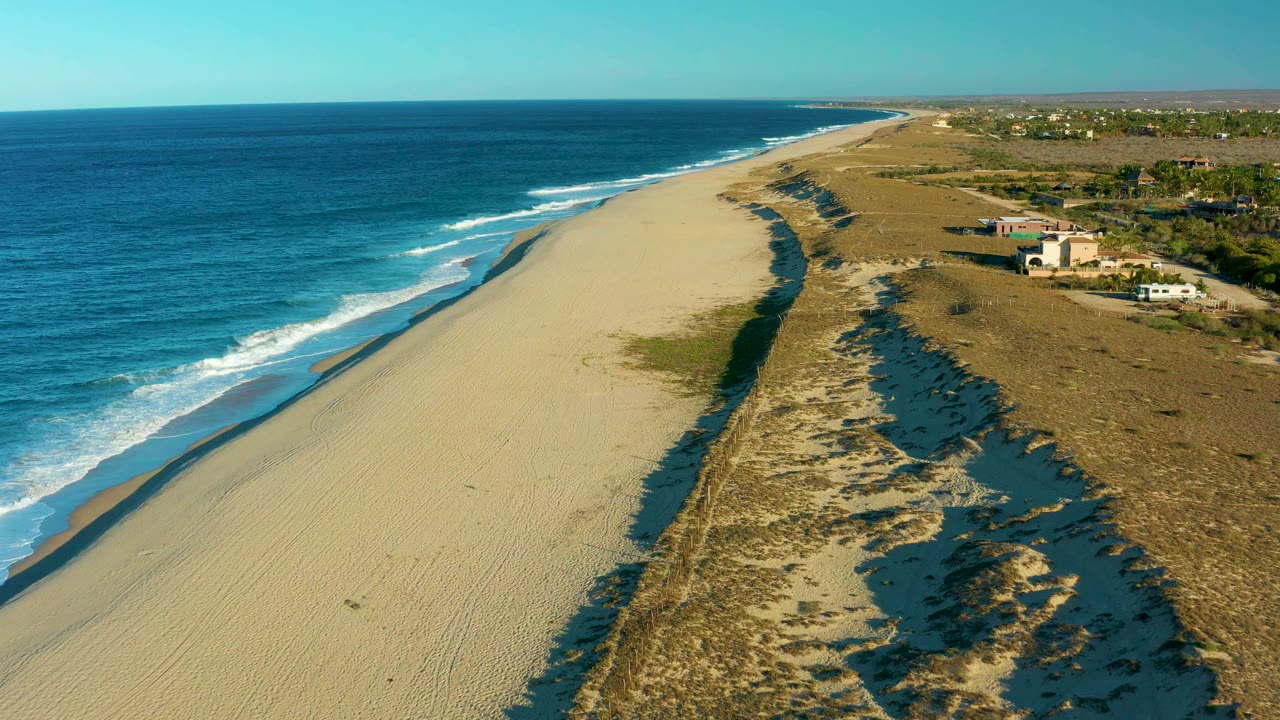 Wide aerial view of surf beside a sandy beach and dune water channels.