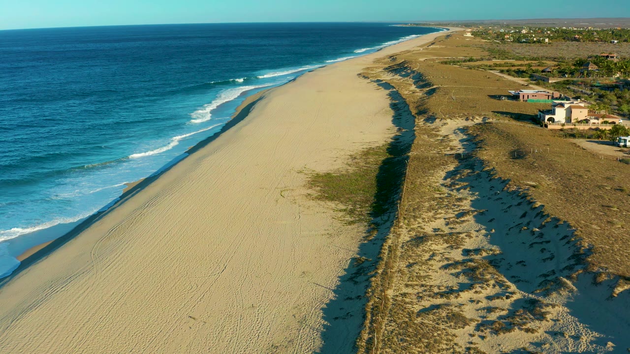 Drone view of white surf rolling toward an empty sandy shore.