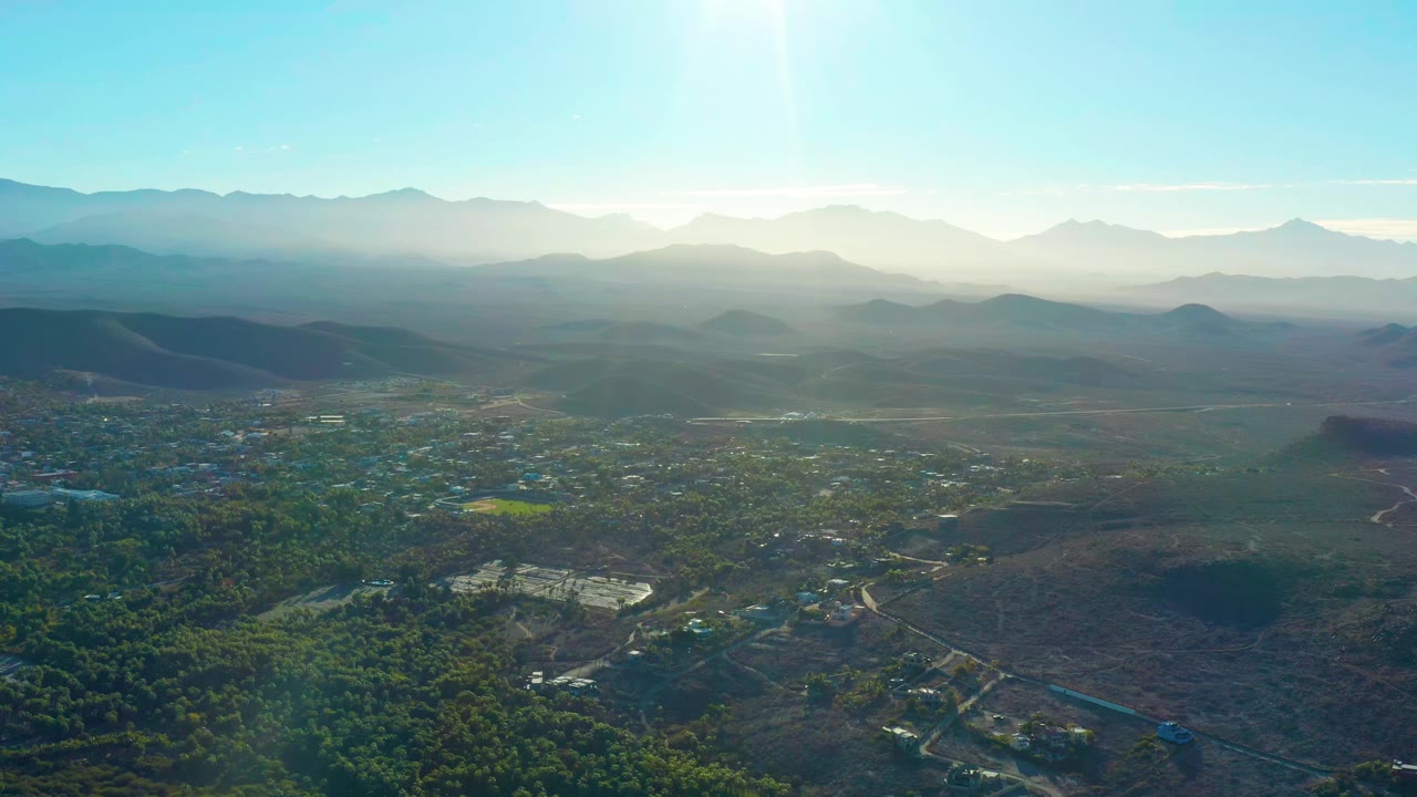 High view across trees, roads, and low hills toward layered mountains.