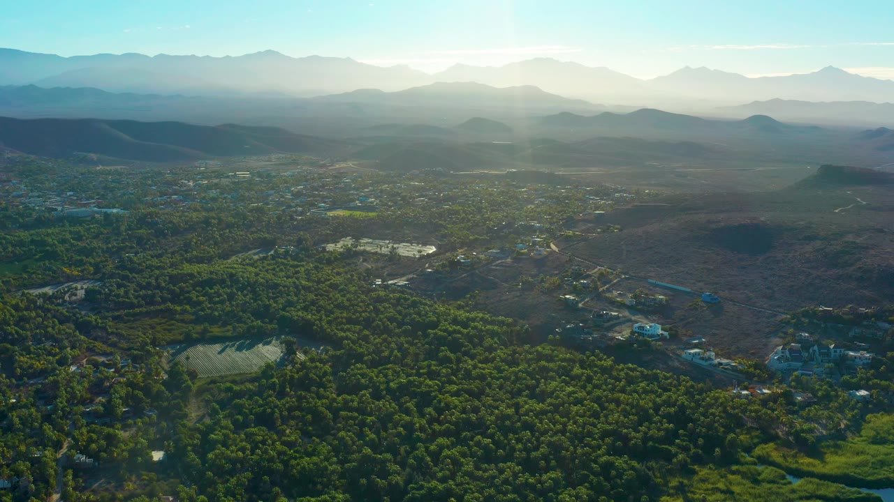 Wide aerial of green valley, small water area, and distant mountains