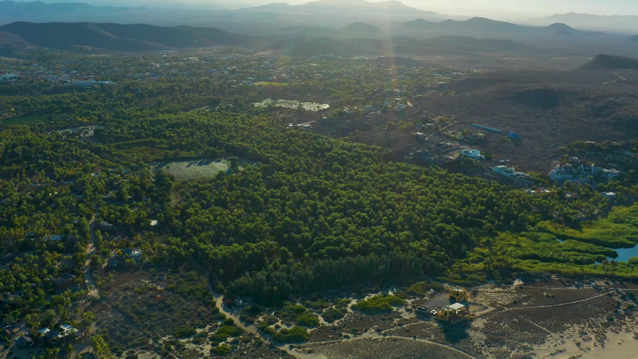Aerial view of forest, open brown land, beach sand, and distant mountains.